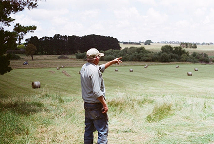 Man wearing a cap in a field, pointing towards something